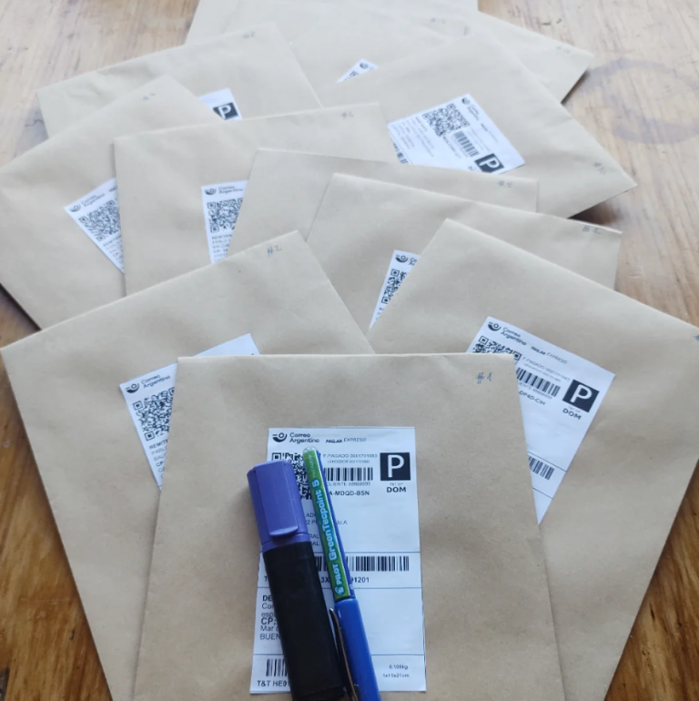 Sobres de papel kraft listos para enviar al correo con sus etiquetas, un resaltador violeta y una lapicera azul